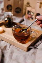 Hand, stirring sugar in a mug of tea. A wooden board, pieces of chocolate and a candle.