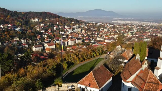Aerial drone view of The Citadel in Brasov at sunrise, Romania. Medieval fortress on the top of a hill. Buildings, yellowed trees, tourists
