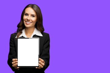 Fototapeta premium Portrait of happy smiling brunette businesswoman showing tablet pc, touchpad, with copy space area for text, isolated over violet purple color background. Confident attractive business woman at studio
