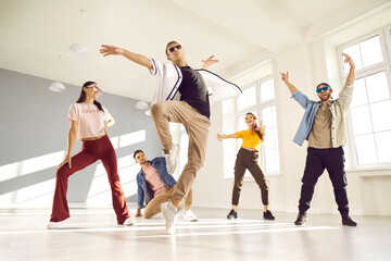 Group of people dancing in modern studio. Energetic male dancer with cool, free attitude, wearing trendy outfit, mixing styles and doing ballet fouette during break dance class with friends, low angle