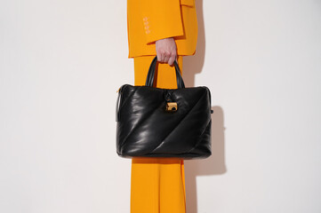 Woman in an orange suit with black leather handbag in her hand on the white background. Quilted...