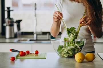 Young woman making salad at the kitchen