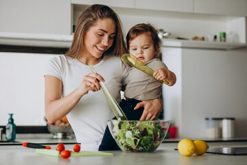 Young mother with her little son making salad at kitchen
