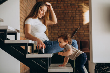 Obraz premium Young mother working from home on laptop with her little son