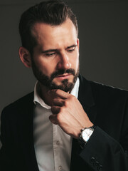 portrait of handsome confident stylish hipster lambersexual model. Sexy modern man dressed in elegant black suit. Fashion male posing in studio on dark background