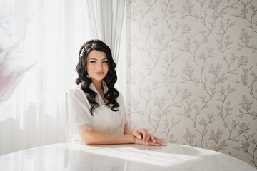 Obraz na płótnie Canvas brunette bride in white silk pajamas with styling and makeup at the table