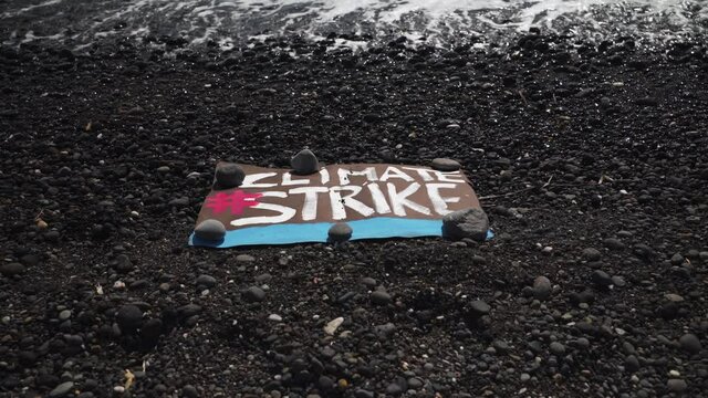 The "Climate Strike" poster lies on the black volcanic sand