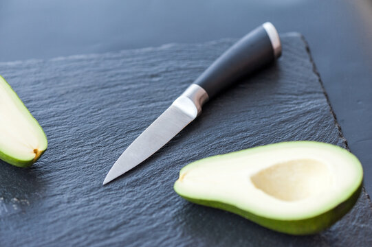 Male hands about to slice the freshly avocado with a chefs kitchen knife on a matte black cutting board. Healthy food and cooking concept