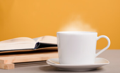 white mug with hot drink, coffee or tea,book, with orange-yellow background