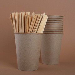 Wooden coffee sticks in a disposable glass. In the background are disposable kraft paper cups. On a brown background