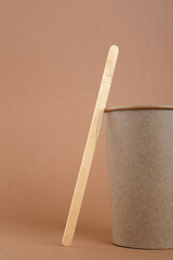Disposable kraft paper cup and wooden coffee stick on brown background