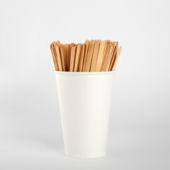 Wooden coffee sticks in a paper disposable cup. On white background
