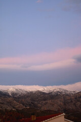 Mountain peaks covered in snow and pink clouds in the sky. Beautiful winter sunset in Croatia.