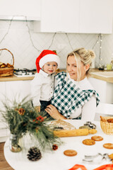 Happy cheerful family mom and little son bake Christmas cookies in a cozy kitchen at home. Christmas preparation, family time. The concept of Christmas and New Year