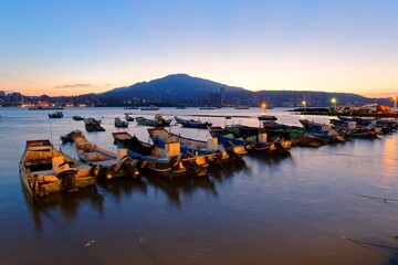 Morning scenery of Tamsui River at sunrise in Bali District, Taipei, Taiwan, with a peaceful view of ferry boats parking on the smooth water & Datun Mountain under beautiful dawning sky in background