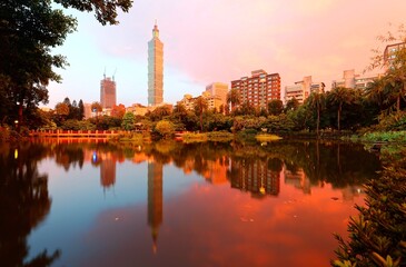 Lakeside scenery of Taipei buildings among skyscrapers in Xinyi District Downtown at dusk with view of reflections on the pond in an urban park ~ Romantic nightscape of Taipei city under rosy sky