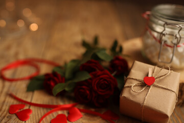 A gift in craft paper on a wooden background, surrounded by red roses, a jar of marshmallows and hearts. Picture for Valentine's Day. The concept of gifts and lovers. High-quality photography