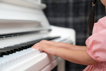 Fototapeta premium Selective focus on the kid finger playing grand piano. Teacher or instructor teach a girl on the class play melody. Close up hand of child. Music with piano. Education and learning concept.