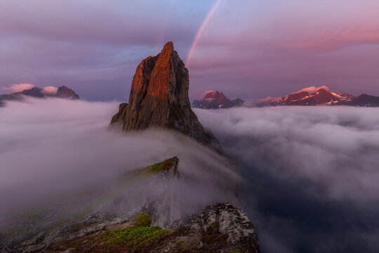 A fabulous view of Mount Segla. The whole scene is lit by sunlight. Fluffy clouds cover the mountains. Epic pink clouds. In the foreground are cliffs and the sea. Top view Norway. Senya Island Europe.