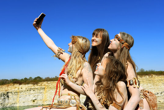 Four girls are dressed up as Neanderthals. One of 
the girls has a mobile phone in her hand and takes 
funny selfie photos of the group.
