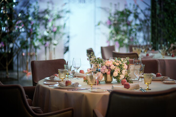 Stylishly decorated dining table. Flowers and glasses are on the festive table. In the foreground is a white plate with a napkin and a red apple in it. Interiors.