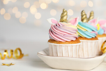 Closeup view of sweet unicorn cupcakes on white table against blurred lights, space for text. Festive treat