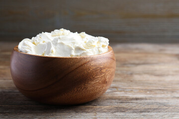 Bowl of tasty cream cheese on wooden table, space for text