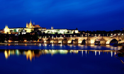 Beautiful scenery of Charles Bridge over Vltava River at blue dusk with the majestic Prague Castle & St. Vitus Cathedral in background and reflections of lights on the water, in Old Town Prague, Czech