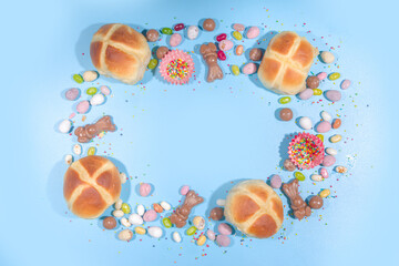 Bright high-colored Easter festive background. Blue background with traditional Easter sweets - hot cross buns, chocolate eggs sweets, colorful sugar sprinkles flatlay copy space