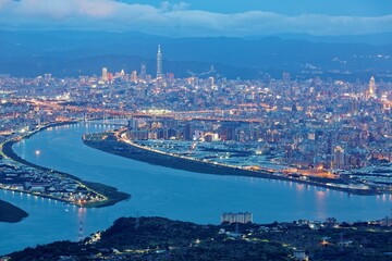 Fototapeta premium Aerial panorama over Taipei, capital City of Taiwan, on a blue gloomy evening with view of the confluence of Tamsui & Keelung River & Taipei 101 Tower among high rise skyscrapers in Downtown at dusk