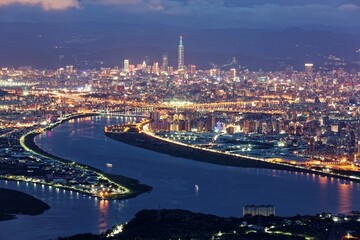 Fototapeta premium Aerial panorama over Taipei, the capital City of Taiwan, on a blue gloomy evening with view of the confluence of Tamsui & Keelung River & Taipei 101 Tower amid highrise skyscrapers in Downtown at dusk
