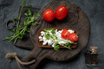 Sandwich for breakfast. Bruschetta with ricotta, tomatoes and micro greens on an old wooden kitchen board and bottle of spices. Healthy food, tasty breakfast, diet concept.