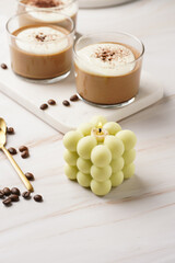 A pale green square bubble candle on a marble kitchen table among coffee beans and sweet dessert - chocolate mouse