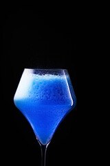 Blue drink is poured into a glass. Black background.