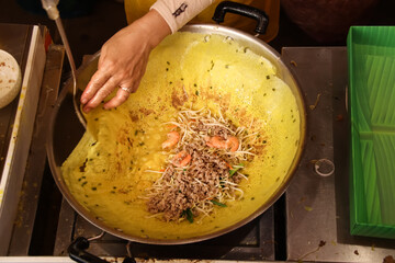 A street food vendor cooking banh xeo (vietnamese crepe), authentic traditional Vietnamese street...