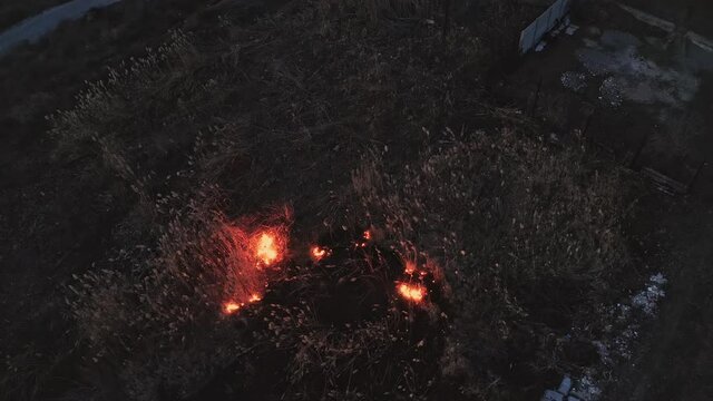 Evening fire in a field near the city. Burning reeds near houses. Seasonal fires in the steppe area. Fire element as a consequence of arbitrary bonfires. Drone video.