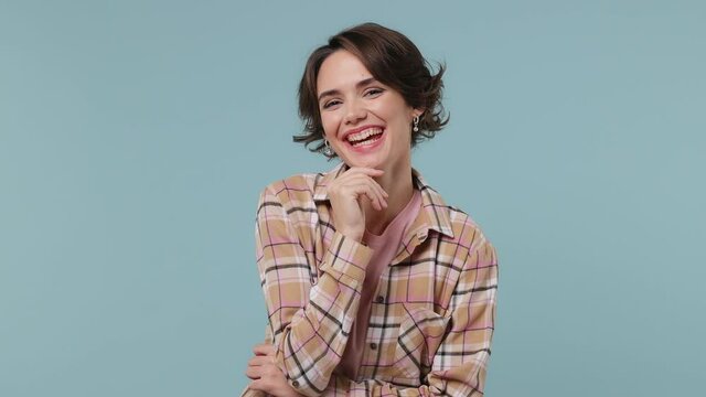 Fun young brunette woman 20s years old wears plaid shirt look around think dream put hand prop up on chin lost in thought and conjectures isolated on pastel plain light blue background studio portrait