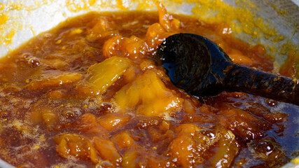 making mango jam, boiling mango pieces with sugar syrup, homemade sweet food with the mixing spoon, closeup view 