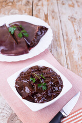 Raw liver on a white plate on a wooden background. Beef liver, top view. Offal in its raw form.
