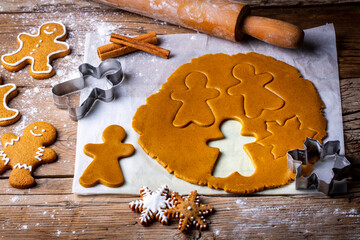 Hand cutting gingerbread dough with christmas metal cutters on wooden board, moody image. Making traditional christmas gingerbread cookies on rustic table with spices, decorations, rolling pin