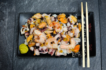 Stir fry noodles with vegetables and shrimps in black bowl. Slate background. Top view.