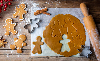 Hand cutting gingerbread dough with christmas metal cutters on wooden board, moody image. Making traditional christmas gingerbread cookies on rustic table with spices, decorations, rolling pin