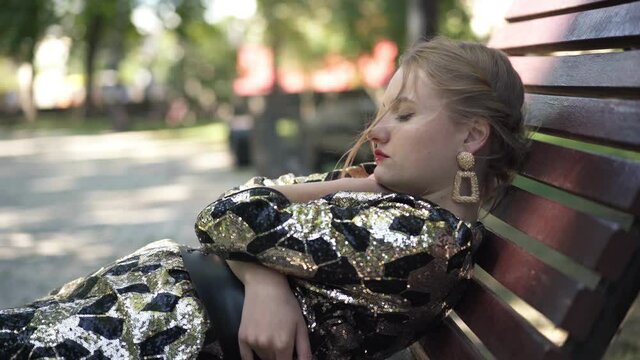 Portrait of tired young woman yawning falling asleep in city park outdoors. Drunk Caucasian millennial party-goer sitting in sunshine closing eyes. Exhaustion and hangover concept