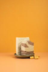 Modern still life. Tasty eastern sweet dessert halva from sunflower seeds, cocoa and tahini on dual color beige background.Traditional dessert confection in Middle East, Balkans and west Asia.Vertical