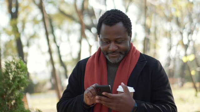 Happy African man looking around and at phone in park outdoors