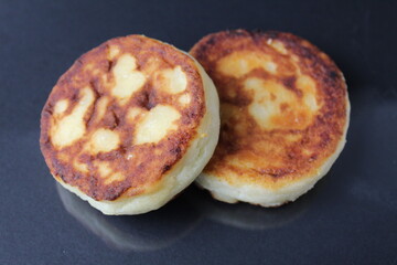 two cheesecakes of cottage cheese pancakes lie on top of each other side by side on a black background with a white sour cream sauce. Delicious healthy breakfast food. healthy eating. diet