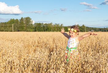 A 5-year-old girl is running across a wheat field and raised her hands to the top. Summer rests outside the city.