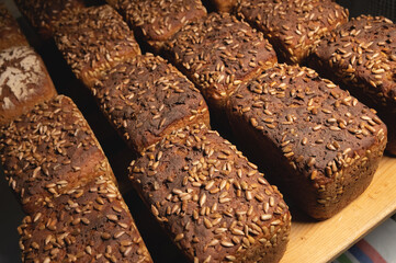 A lot of whole delicious homemade rectangular rye bread with sunflower seeds on top lies on a wooden rack background