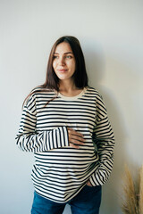 Vertical portrait of a young pregnant woman in a striped sweatshirt.