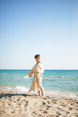 Practice on the beach. A boy in a muslin robe on the background of the sea is doing energy exercises.